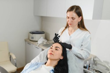 Doktor saç dökülmesinden bir kızın kafasına enjeksiyon yapıyor. Kozmetik kliniğinde saç tedavisi.