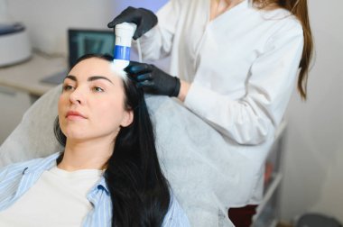 Kuaför saçlarını kontrol ediyor. Tanısal saç ve kafa derisi. Trihoskopiya. Doktor hasta kadın saçlarını özel bir cihaz ve bilgisayar ile muayene etti.