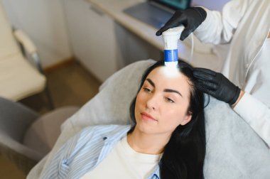 Kuaför saçlarını kontrol ediyor. Tanısal saç ve kafa derisi. Trihoskopiya. Doktor hasta kadın saçlarını özel bir cihaz ve bilgisayar ile muayene etti.