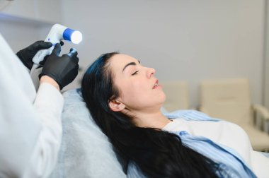 Kuaför saçlarını kontrol ediyor. Tanısal saç ve kafa derisi. Trihoskopiya. Doktor hasta kadın saçlarını özel bir cihaz ve bilgisayar ile muayene etti.