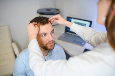 Bir tricholog, saç dökülmesine başlayan bir adamın saçını inceliyor. Bir dermatologla görüşeceğim. Saç dökülmesi, alopezi, pruritus, yanmakta olan kafa ya da sebora.