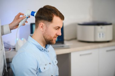 Genç bir adam trikop ile incelenir kafa derisi ve saç folikülleri durumu.