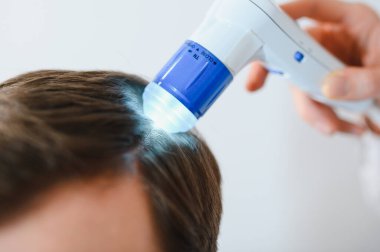 Genç bir adam trikop ile incelenir kafa derisi ve saç folikülleri durumu.