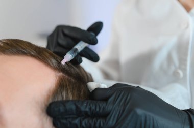 Adam kuaförde kuaförlük yapıyor, mezoterapi seansı yapıyor. Kadın terapist koruyucu eldiven verip şırınga yapıyor..