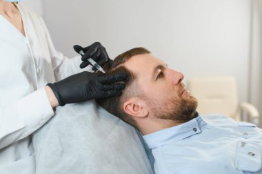 Yakışıklı bir adamın kuaförde saç bakımına gidişinin yan görüntüsü. Adam estetik kliniğinde mezoterapi görüyor, terapist eldiven takıyor kafa derisine iğne yapıyor, yakın çekim yapıyor.