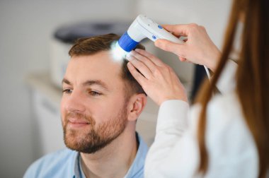 Genç bir adam trikop ile incelenir kafa derisi ve saç folikülleri durumu.