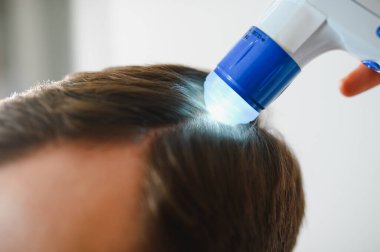 Genç bir adam trikop ile incelenir kafa derisi ve saç folikülleri durumu.