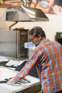Donmuş balıklı sakallı adam elleri dondurulmuş gıda bölümündeki buzdolabının yanında duruyor..