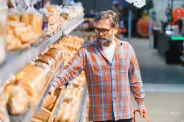 Süpermarketin bakkal bölümünden fırın ürünlerini seçen yaşlı bir adam. Boşluğu kopyala