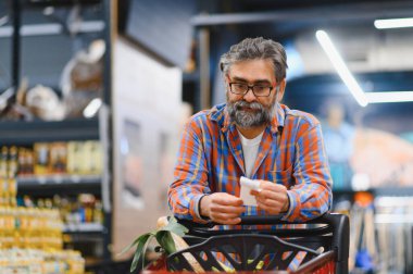 Süpermarketteki fiyatları kontrol etmek için yaşlı adamın elinde fatura var..