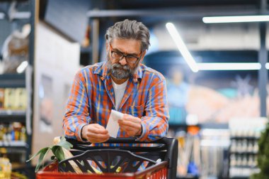Süpermarketteki fiyatları kontrol etmek için yaşlı adamın elinde fatura var..
