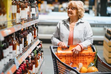 Yaşlı kadın alıcı marketten bir şişe şarap ya da şampanya seçiyor.