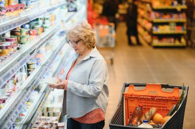 Alışveriş merkezinde alışveriş yapan yaşlı bir kadının portresi. Düşük açılı çekim. Yaşlı bayan market alışverişi yapıyor..