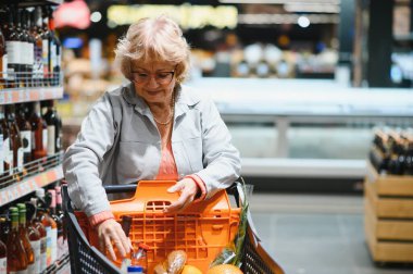 Yaşlı kadın alıcı marketten bir şişe şarap ya da şampanya seçiyor.