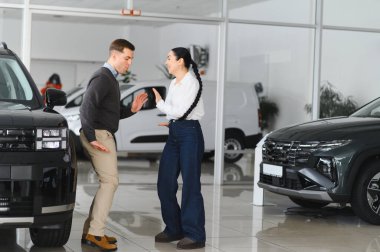 Şen şakrak bir çift genç kadın ve erkek galeride yeni araba aldıktan sonra dans ediyorlar..