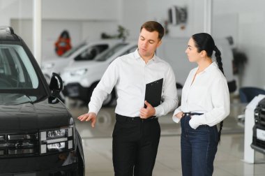 Güzel genç kadın yakışıklı araba Bayilik işçi için bir araba içinde Bayilik seçerken konuşuyor.