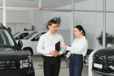 Satıcı otomobil merkezinde bayan müşteriye yeni araba gösteriyor.