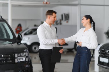 Genç beyaz kadın bir bayiden araba satın alıyor. Sakallı satıcı arabanın anahtarlarını verir..