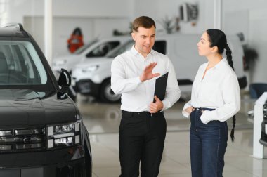 Satıcı otomobil merkezinde bayan müşteriye yeni araba gösteriyor.