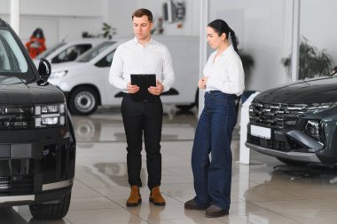 Satıcı otomobil merkezinde bayan müşteriye yeni araba gösteriyor.