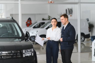 Dost canlısı bayan araba satıcısı lüks araba galerisinde duruyor ve bir müşteriyle görüşüyor..