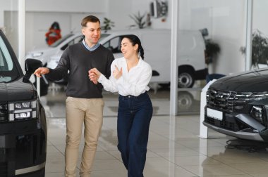 Mutlu genç çift aile için yeni bir araba seçer ve alır. Galeriyi ziyaret ediyorum..