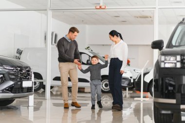 Araba galerisinde bir aile. Mutlu bir aile galeride bir araba satıcısıyla anlaşma yapmış. Mutlu aile galeride yeni bir araba seçiyor.