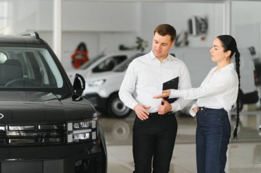 Güzel genç kadın yakışıklı araba Bayilik işçi için bir araba içinde Bayilik seçerken konuşuyor.