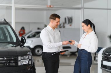 Beyaz bir kadın araba galerisinden araba satın alıyor. Sakallı satıcı arabanın anahtarlarını verir..