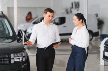 Satıcı otomobil merkezinde bayan müşteriye yeni araba gösteriyor.