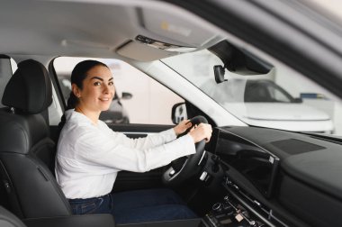 Yeni kırmızı aracın içinde otururken gülümseyen ve kameraya bakan neşeli bayan bir araba satıcısı.