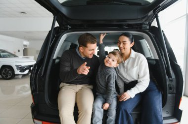 Genç ve mutlu bir aile, galeride yeni bir araba alırken eğleniyor..
