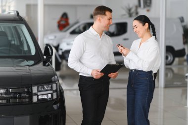 Genç beyaz kadın bir bayiden araba satın alıyor. Sakallı satıcı arabanın anahtarlarını verir..