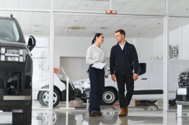 Dost canlısı bayan araba satıcısı lüks araba galerisinde duruyor ve bir müşteriyle görüşüyor..