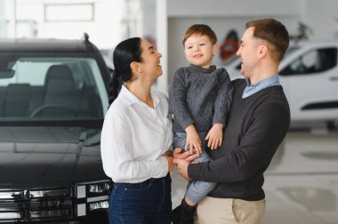 Genç ve mutlu bir aile, galeride yeni bir araba alırken eğleniyor..
