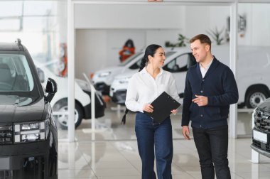 Dost canlısı bayan araba satıcısı lüks araba galerisinde duruyor ve bir müşteriyle görüşüyor..