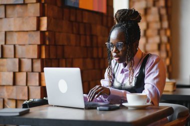 Cep telefonlu akıllı genç bir kadının portresi açık kahve dükkanında dizüstü bilgisayarla çalışıyor..