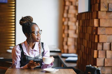 Modern bir kafede akıllı telefon kullanan gülümseyen bir kadın..