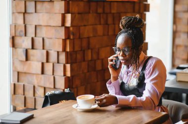 Modern bir kafede akıllı telefon kullanan gülümseyen bir kadın..