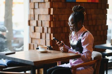 Genç Afrikalı bir kadın modern bir kafede akıllı telefon kullanıyor..