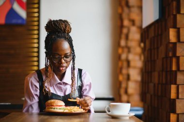 Afro saçlı Afrikalı bir kadın leziz bir klasik burgerle patates kızartması yiyor. Hile Yemeği.