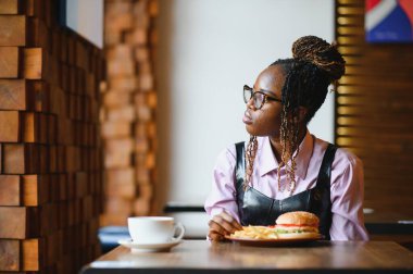 Afro saçlı Afrikalı bir kadın leziz bir klasik burgerle patates kızartması yiyor. Hile Yemeği.