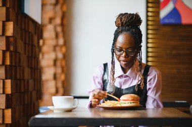 Afro saçlı Afrikalı bir kadın leziz bir klasik burgerle patates kızartması yiyor. Hile Yemeği.