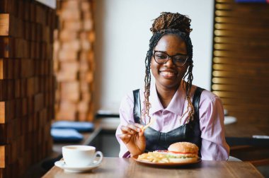 Afro saçlı Afrikalı bir kadın leziz bir klasik burgerle patates kızartması yiyor. Hile Yemeği.