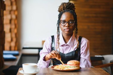 Afro saçlı Afrikalı bir kadın leziz bir klasik burgerle patates kızartması yiyor. Hile Yemeği.