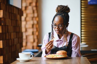 Afro saçlı Afrikalı bir kadın leziz bir klasik burgerle patates kızartması yiyor. Hile Yemeği.