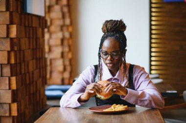 Kafede hamburger ve patates yiyen Afrikalı bir kız. Fast food konsepti.