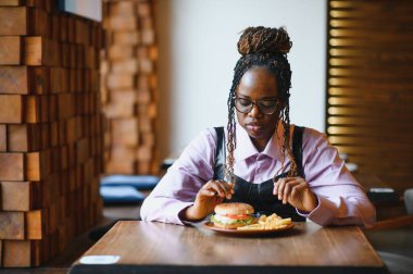 Afro saçlı Afrikalı bir kadın leziz bir klasik burgerle patates kızartması yiyor. Hile Yemeği.