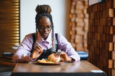 Afro saçlı Afrikalı bir kadın leziz bir klasik burgerle patates kızartması yiyor. Hile Yemeği.