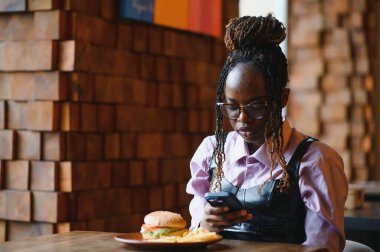 Afro saçlı Afrikalı bir kadın leziz bir klasik burgerle patates kızartması yiyor. Hile Yemeği.